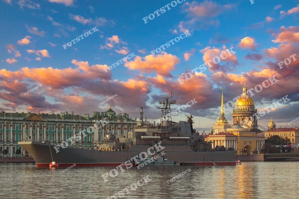 На фотографии изображен военный корабль, стоящий на Неве, с величественными зданиями Исаакиевского собора и Эрмитажа на заднем плане. Эта сцена подчеркивает важность военно-морского флота России, а также подготовку к параду, символизируя мощь и торжественность. Военные корабли на реке и историческая архитектура создают эффектный контраст, подчеркивая уникальную атмосферу Санкт-Петербурга.